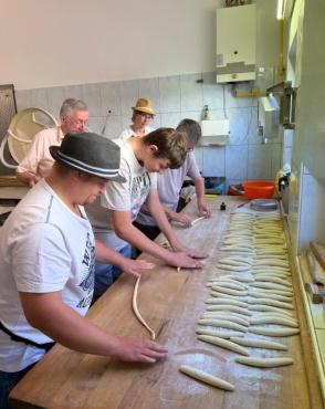 F&uuml;nf Personen formen Teigst&uuml;cke auf einem langen Holztisch in einer B&auml;ckerei.