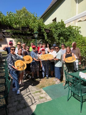 Eine Gruppe von Menschen l&auml;chelt in die Kamera. Einige halten gro&szlig;es Geb&auml;ck in Hutform und ein Tablett mit gebackenen Br&ouml;tchen in Form einer Blume.