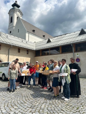 Eine Gruppe von Menschen steht vor einer Kirche und lächelt in die Kamera. Einige halten Tabletts mit Gebäck.