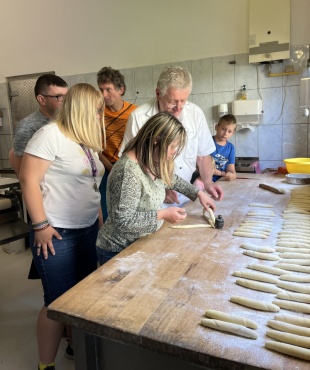 Fünf Personen formen Teigstücke auf einem großen Holztisch in einer Bäckerei.