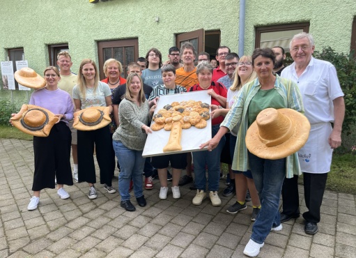 Eine Gruppe von Menschen lächelt in die Kamera. Einige halten großes Gebäck in Hutform und ein Tablett mit gebackenen Brötchen in Form eines Baums.