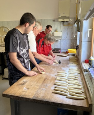 Vier Personen formen Teigstücke auf einem langen Holztisch in einer Bäckerei.