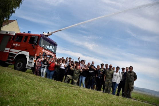 Eine Gruppe von Menschen steht auf einer Wiese vor einem Feuerwehrfahrzeug.