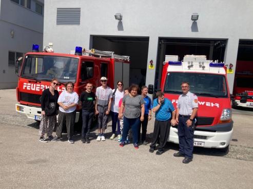 Eine Gruppe von Menschen posiert vor zwei roten Feuerwehrfahrzeugen und l&auml;chelt in die Kamera.
