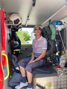Ein Mann sitzt im Inneren eines Feuerwehrfahrzeugs und l&auml;chelt in die Kamera.