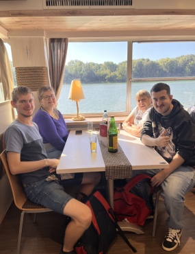 Vier Personen sitzen am Tisch und l&auml;cheln in die Kamera.