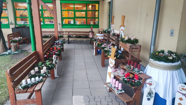 Adventskr&auml;nze und verschiedene Dekorationsartikel ausgestellt auf mehreren Holzb&auml;nken.