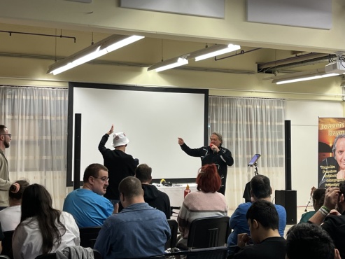 Eine Gruppe von Menschen sitz und h&ouml;rt einem Mann beim Singen zu.