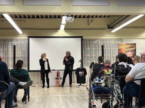 Eine sitzende Gruppe von Menschen schaut zwei Personen beim Singen zu.