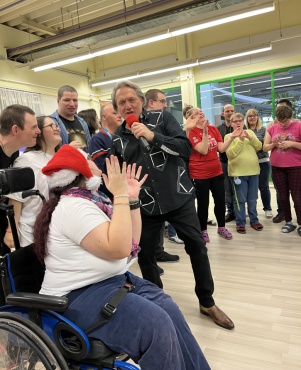 Eine Gruppe von Menschen beim Tanzen. Ein Mann h&auml;lt ein Mikrofon und singt.