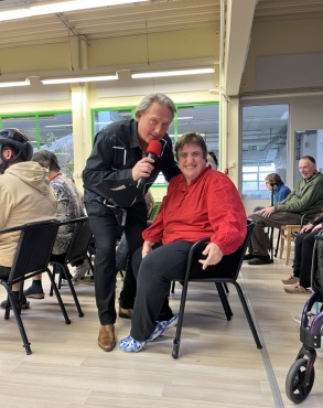 Ein Mann mit einen Mikrofon und eine sitzende Frau l&auml;cheln in die Kamera.