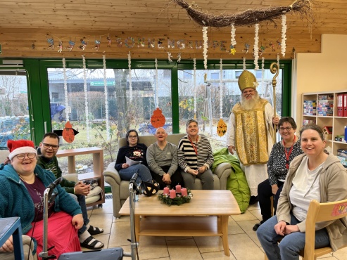 Eine sitzende Gruppe von Menschen posiert gemeinsam mit dem Nikolaus und l&auml;chelt in die Kamera.