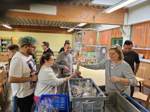 Eine Gruppe von Menschen steht in der Reihe und bekommt Geschenksackerl von einer Frau &uuml;berreicht.