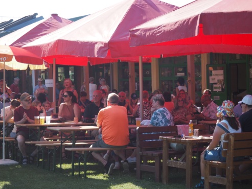 Menschen sitzen an Gartengarnituren und Heurigenb&auml;nken im Garten.