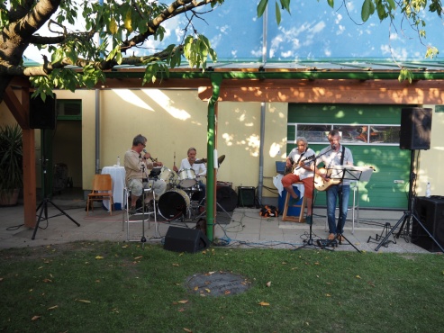 4 Männer musizieren auf verschiedenen Instrumenten im Garten.