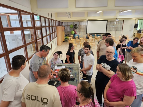 Eine Gruppe von Menschen steht um einen Tischfußball-Tisch, während ein Mann Autogrammkarten unterschreibt.