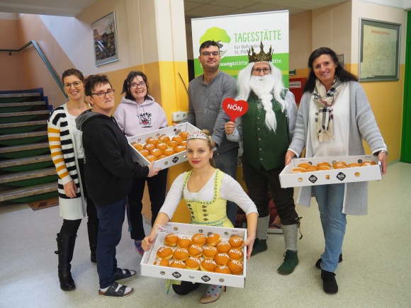 7 Personen lächeln in die Kamera. Sie halten 3 Schachteln mit Krapfen.